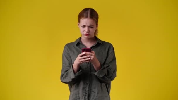 黄色の背景で彼女の携帯電話を使用して女性の4Kビデオ 感情の概念 — ストック動画