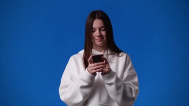 4k video of one girl typing text and looking up on blue background. Concept of emotions.