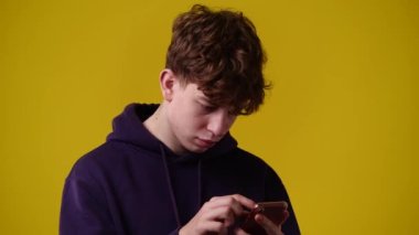 4k video of one curly man looking for something on his phone and smiling with a thumbs up on yellow background. Concept of emotions.