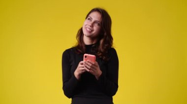 4k video of one woman typing text and looking up on yellow background. Concept of emotions.