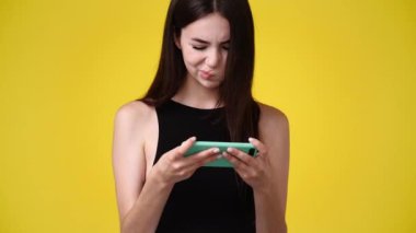 4k video of one girl is playing on the phone over yellow background. Concept of emotions.