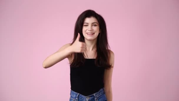 ピンクの背景に親指を立てて微笑む1人の少女の4Kスローモーションビデオ 感情の概念 — ストック動画