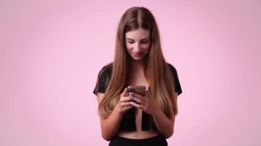 4k video of one girl typing text and looking up laughingly on pink background. Concept of emotions.