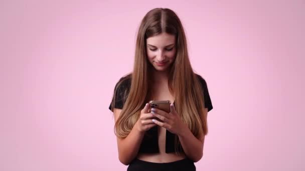 4K视频 一个女孩打字 笑着抬头看粉色背景 情绪的概念 — 图库视频影像