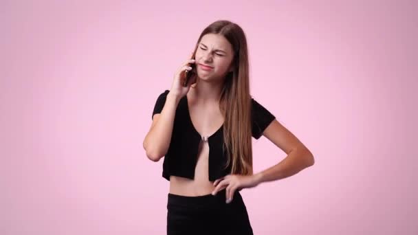 4K视频 一个女孩在电话里用粉色背景的负面面部表情说话 情绪的概念 — 图库视频影像