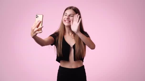 1人の女の子の4Kビデオはピンクの背景の上に彼女の電話でビデオを作ります 感情の概念 — ストック動画