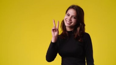 4k video of one woman showing two fingers over yellow background. Concept of emotions.