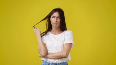 4k video of one girl with negative facial expression touching her hair on yellow background. Concept of emotions.