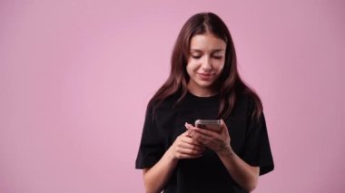 Pembe arka planda telefonunu kullanan bir kızın 4K videosu. Duyguların kavramı.