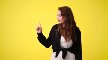 4k video of one girl pointing at left over yellow background. Concept of emotions.