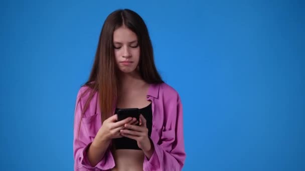 1人の女の子の4K動画がテキストを入力し 青の背景に笑いながら離れて見えます 感情の概念 — ストック動画