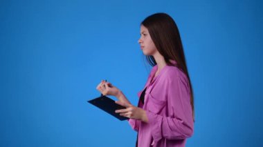 4k video of one girl which thinks and notes something with a pen on tablet over blue background. Concept of emotions.