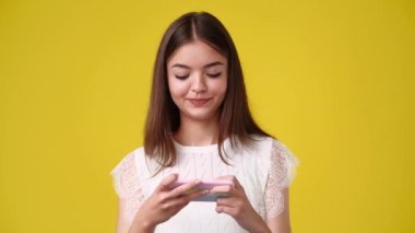 4k video of one girl is playing on the phone over yellow background. Concept of emotions.