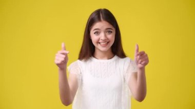 4k video of one girl pointing at someone and showing thumbs up over yellow background. Concept of emotions.