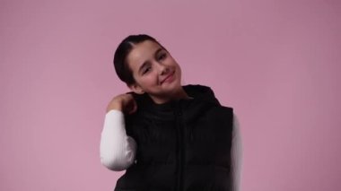 Genç bir kızın 4K videosu saçını kıvırıyor ve mavi arkaplanda bir video için poz veriyor. Duyguların kavramı.