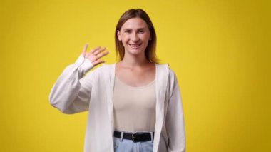 4k video of one girl waving her hands and smiling over yellow background. Concept of emotions.
