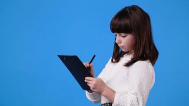 Bir genç kızın 4k videosu mavi arka planda bir tablet üzerinde bir kalemle bir şeyler düşünüyor ve not alıyor. Duyguların kavramı.