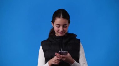 4k video of one young girl typing text and smiles on blue background. Concept of emotions.