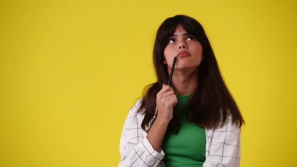 Video Una Chica Piensa Poner Bolígrafo Barbilla Sobre Fondo Amarillo — Vídeo de stock