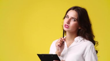 4k video of one woman which thinks and notes something with a pen on tablet over yellow background. Concept of emotions.