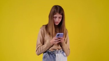4k video of one girl typing text and looking up on yellow background. Concept of emotions.