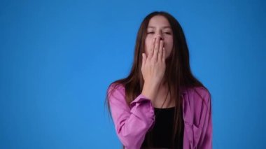 Mavi arka planda hava öpücüğü gönderen bir kızın 4K videosu. Aşk duygusu kavramı.