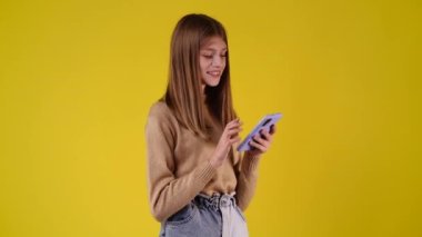 Sarı arka planda telefonunu kullanan bir kızın 4K videosu. Duyguların kavramı.