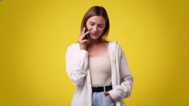 Sarı arka planda telefonla konuşan bir kızın 4K videosu. Duyguların kavramı.