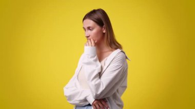 Sarı arka planda düşünceli yüz ifadesi olan bir kızın 4K videosu. Fikirleri olan kız kavramı.