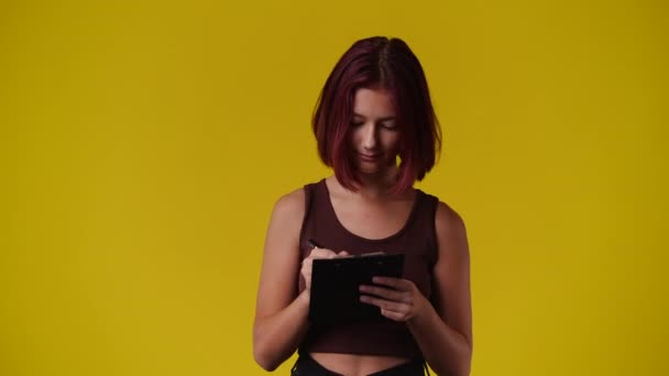 黄色の背景の上にノートを取る1人の女の子の4Kビデオ 感情の概念 — ストック動画