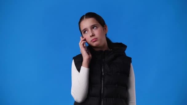 青い背景で電話で話している1人の少女の4Kビデオ 感情の概念 — ストック動画