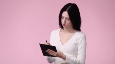 4k video of one girl taking down some notes over pink background. Concept of emotions.