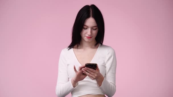 ピンクの背景の上に彼女の携帯電話を使用して1人の女の子の4Kビデオ 感情の概念 — ストック動画