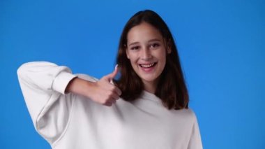 4k video of one girl pointing at right and showing thumb up over blue background. Concept of emotions.