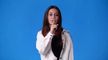 4k video of one girl showing silence sign on blue background. Concept of emotions.