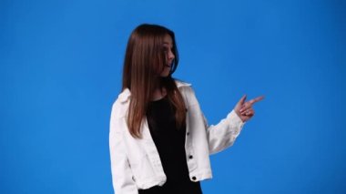 4k video of one girl pointing at right and showing thumbs up on blue background. Concept of emotions.