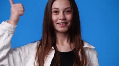 4k slow motion video of one girl pointing at the camera and showing thumbs up over blue background. Concept of emotions.