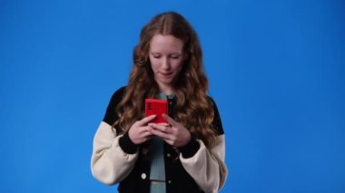Mavi arka planda telefonla konuşan bir kızın 4K videosu. Duyguların kavramı.