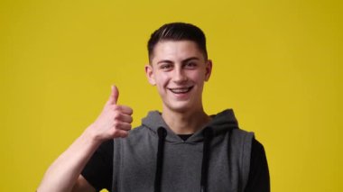 Sarı arka planda baş parmağını gösteren bir adamın 4K videosu. Duyguların kavramı.