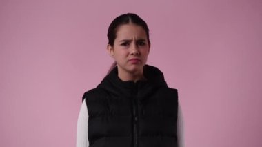 Pembe arka planda negatif yüz ifadesi olan birini durduran bir kızın 4K yavaş çekim videosu. Duyguların bütünlüğü.