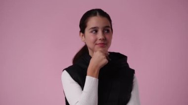 Bir kızın bir şey düşündüğü ve pembe arka planda baş parmağını gösterdiği 4K video. Duyguların kavramı.