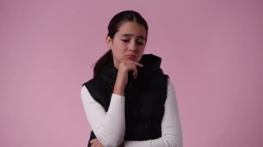 Bir şey düşünen ve pembe arka planda çenesini tutan bir kızın 4K videosu. Duyguların kavramı.