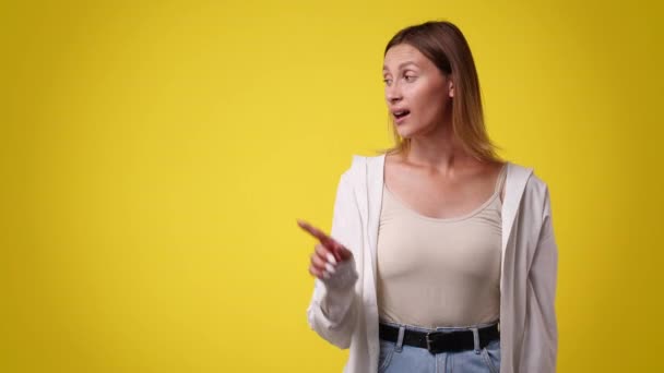一个面部表情正面的女孩的4K慢动作视频指向左边 并在黄色背景上显示大拇指向上 情绪的概念 — 图库视频影像