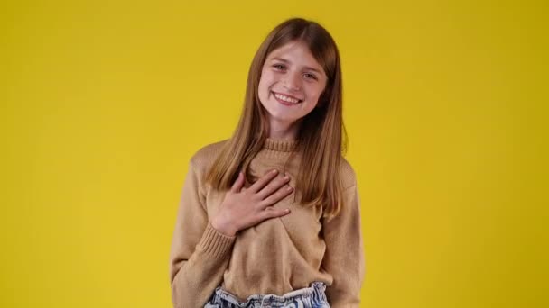 4K视频 一个快乐的女孩笑了 并把他的头发固定在黄色背景 情绪的概念 — 图库视频影像