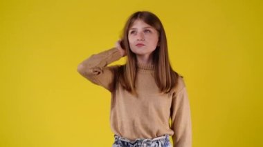4k video of one girl fixes his hair and thinking about something over yellow background. Concept of emotions.
