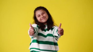 4k video of one girl showing thumbs up and smiling over yellow background. Concept of emotions.