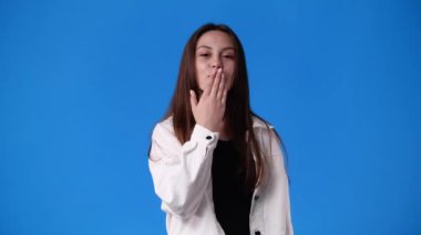 Gülümseyen bir kızın 4K videosu ve mavi arka planda bir hava öpücüğü gönderiyor. Duyguların kavramı.