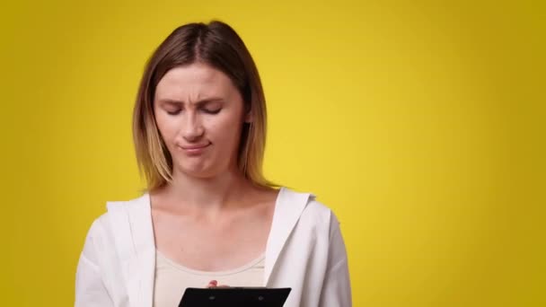 黄色の背景の上にタブレットにペンで何かを考え メモする1人の女の子の4Kビデオ 感情の概念 — ストック動画