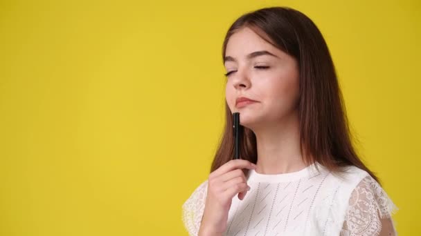 黄色の背景の上にペンで何かを考えている1人の少女の4Kビデオ 感情の概念 — ストック動画
