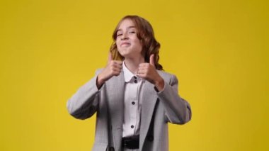 4k video of one girl showing thumbs up and smiling over yellow background. Concept of emotions.